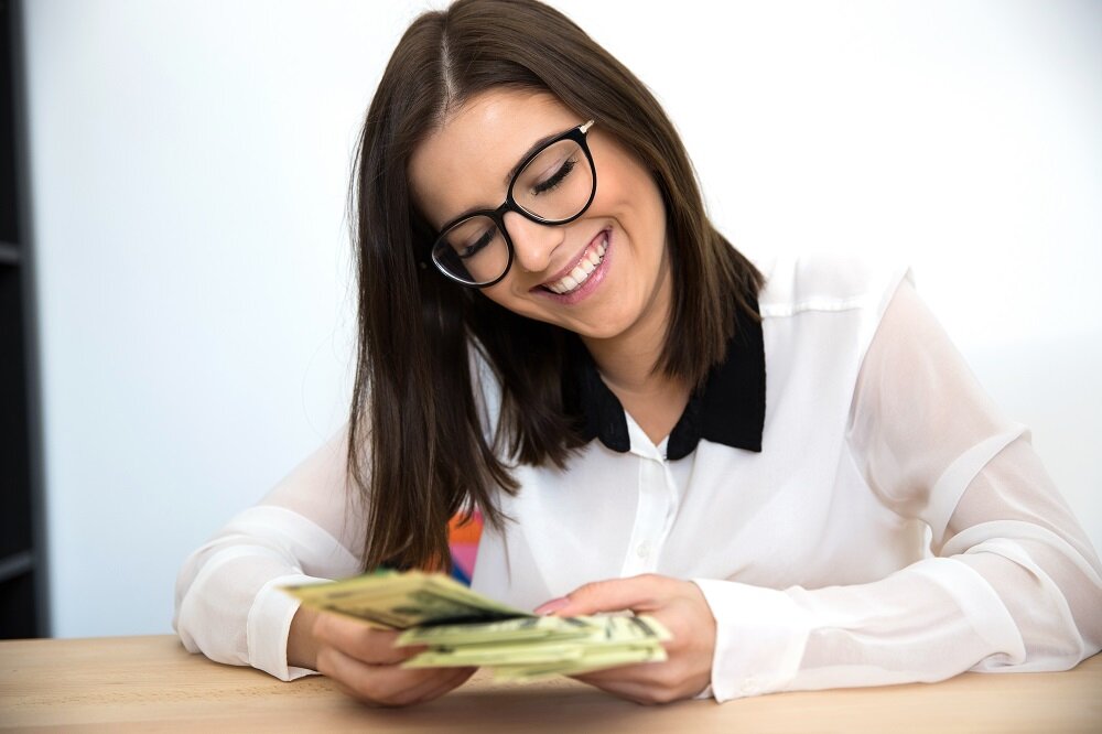 Cheerful businesswoman sitting at the table and holding money